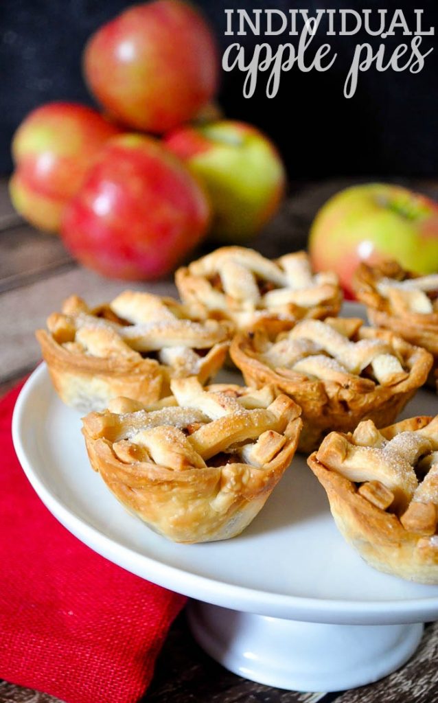 Individual Apple Pies on a white cake stand with apples.