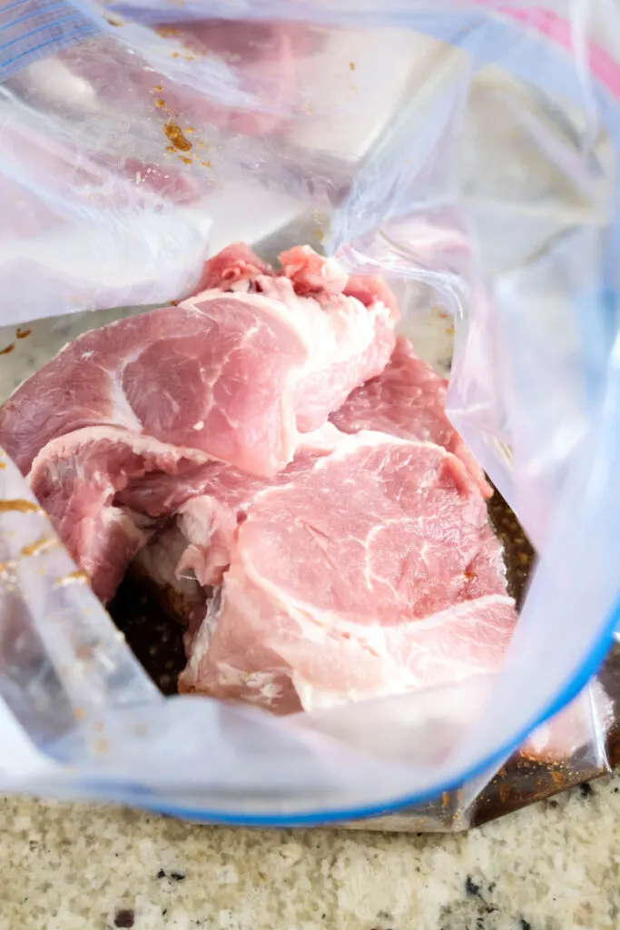 Overhead view of an open plastic bag filled with pork shoulder and marinade