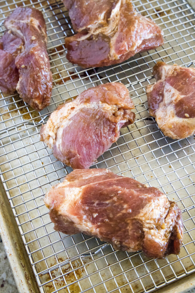 Overhead view of five pieces of marinated pork on a wire rack on a baking sheet