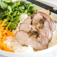 Close up of sliced char siu pork in a bowl on top of rice with carrots and spinach