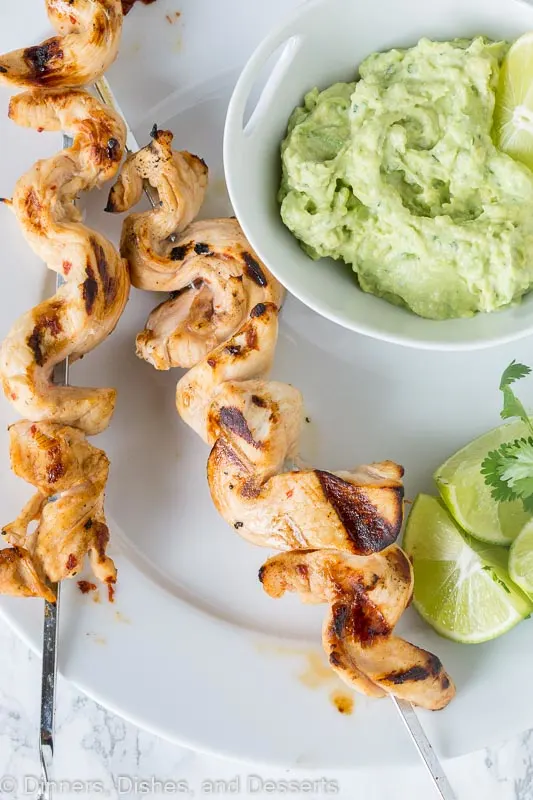 grilled chicken on skewers with avocado dipping sauce on a plate