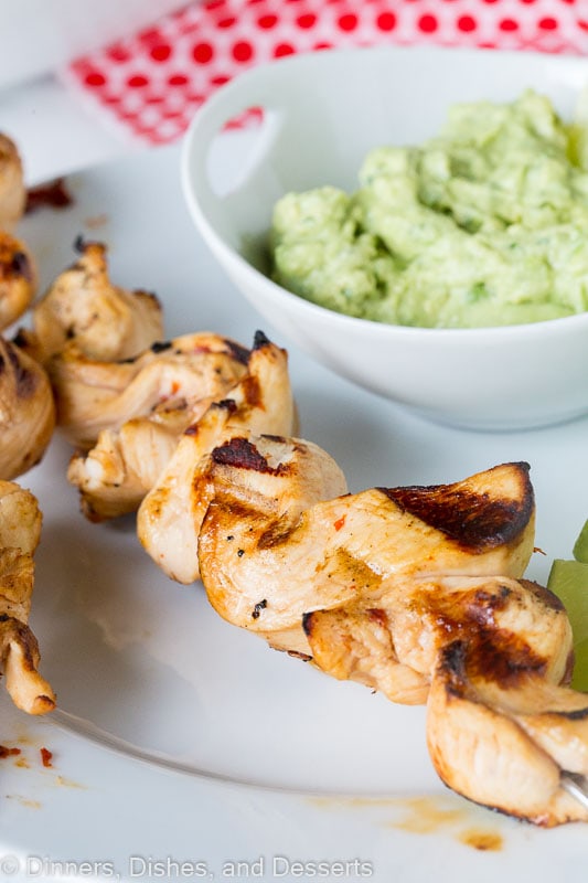 grilled chicken on skewers with avocado dipping sauce on a plate