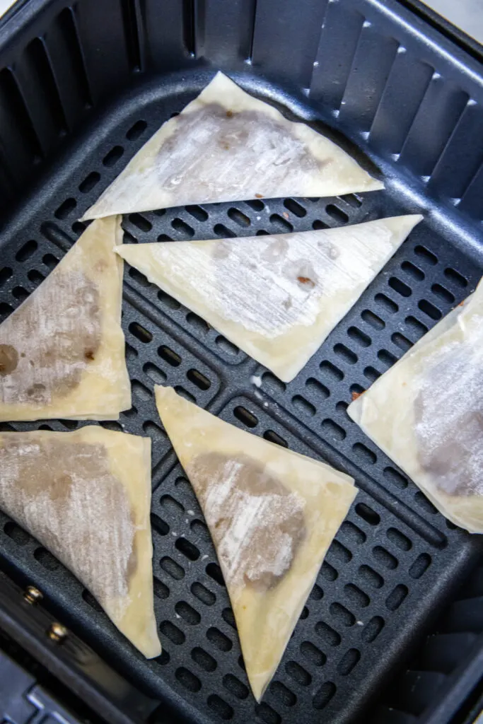 Six uncooked wonton wrappers filled with Nutella in an air fryer basket