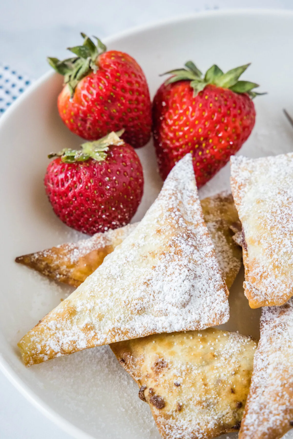 Overhead view of a few wontons covered in powdered sugar, next to three strawberries