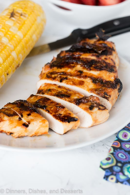 sliced barbecue chicken on a plate next to corn on the cob