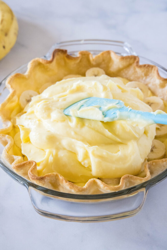 A spatula spreading banana cream pie filling into a pastry shell