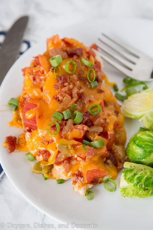 A close up of a plate of food with chicken topped with tomatoes, bacon and melted cheese