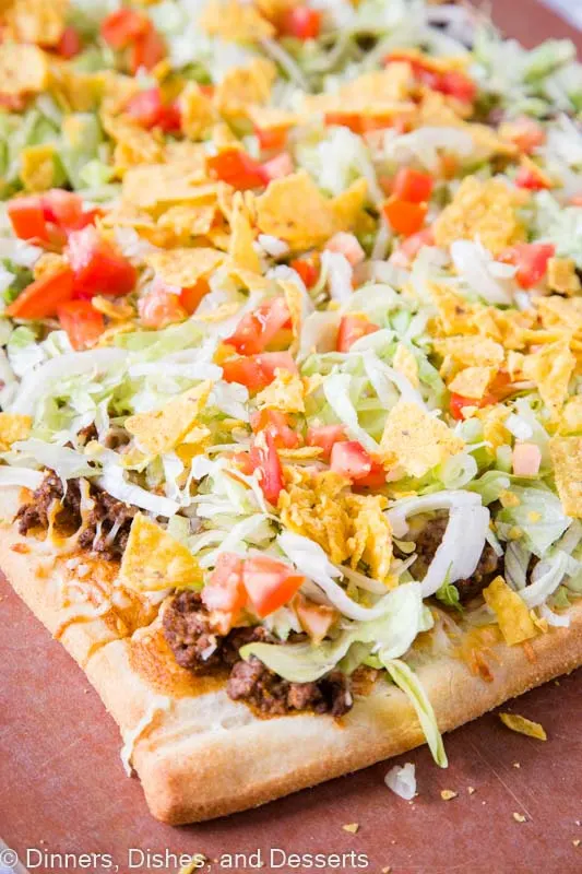 Taco pizza with refried beans, taco sauce, taco meat, cheese, lettuce, tomatoes and tortilla chips!