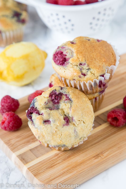 a raspberry muffin on a wooden board with lemon and raspberries next to it