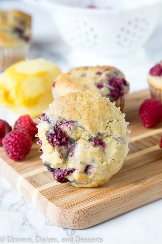 a raspberry muffin on a wooden board with raspberries and lemon next to it
