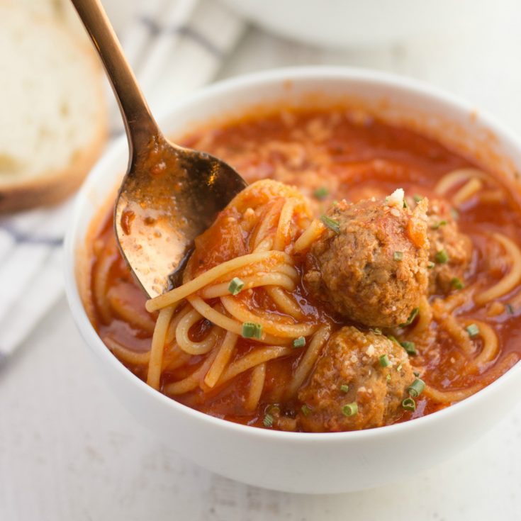spaghetti and meatball soup in a bowl with a spoon