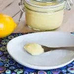 lemon curd on spoon on white plate with lemons on background