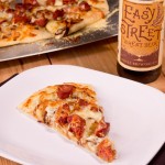 Caramleized Onion and Andouille Pizza on white plate with beer in backgruond