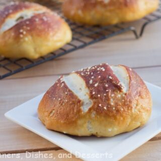 pretzel roll on plate with rolls on cooling rack in background