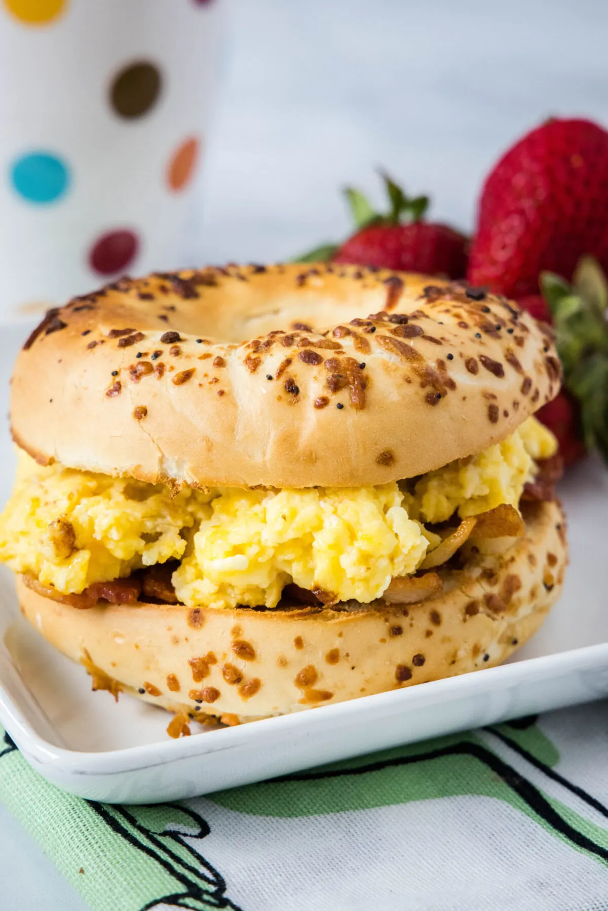 A bagel sandwich with eggs on a plate with strawberries