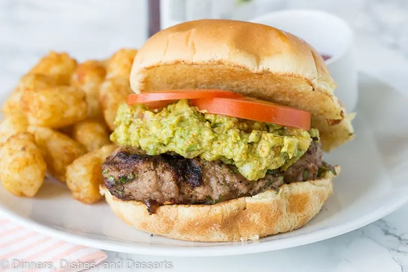 A turkey burger topped with guacamole and tomato on a plate