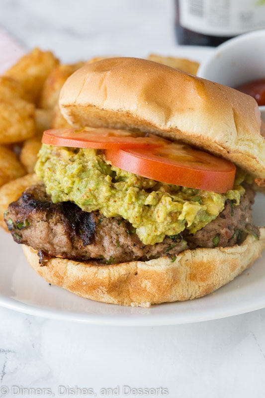 A close up of a turkey burger topped with guacamole and tomato on a plate