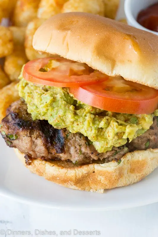A close up of a turkey burger topped with guacamole and tomato on a plate
