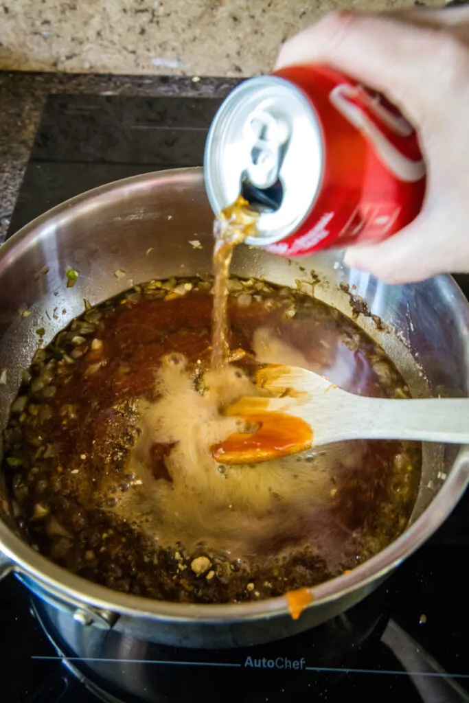 A can of coke being poured into a pot of BBQ sauce