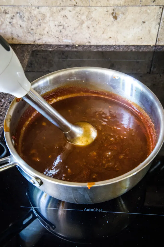 An immersion blender blending BBQ sauce in a pot