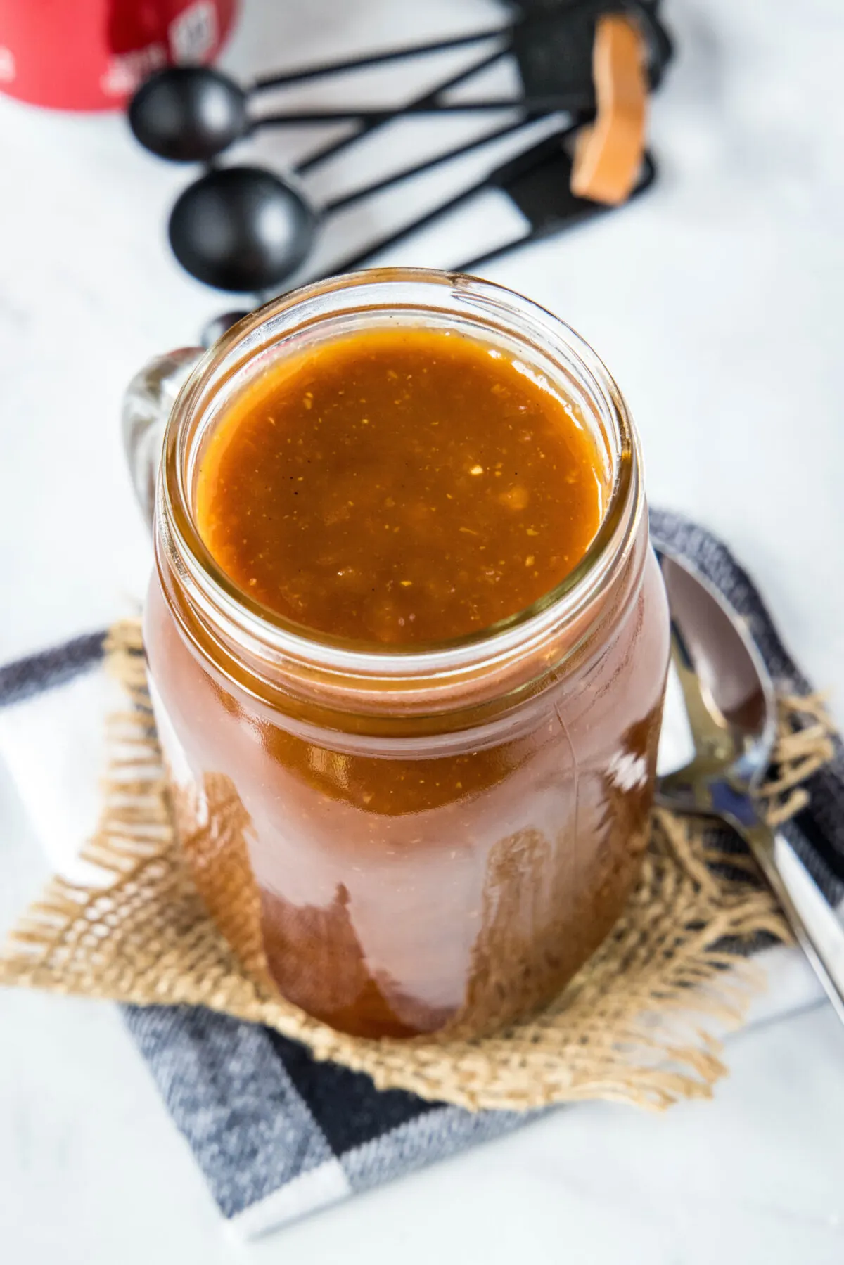 Overhead view of a jar of BBQ sauce next to a spoon and measuring spoons