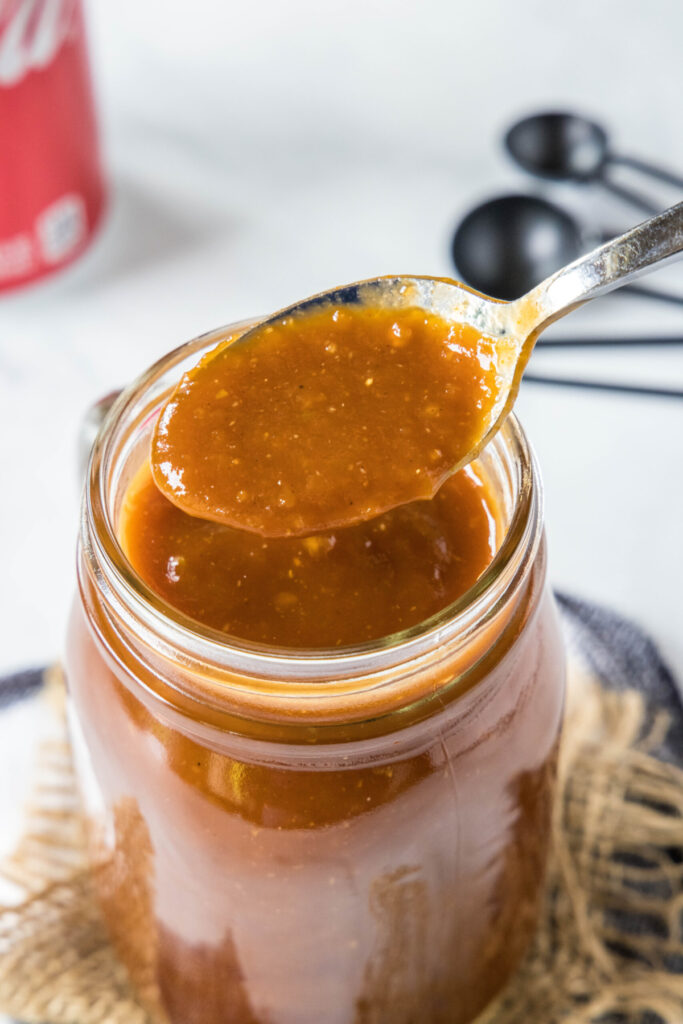 Close up of a spoonful of BBQ sauce above a jar of BBQ sauce
