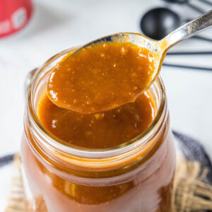 Close up of a spoon pulling out a spoonful of BBQ sauce from a jar