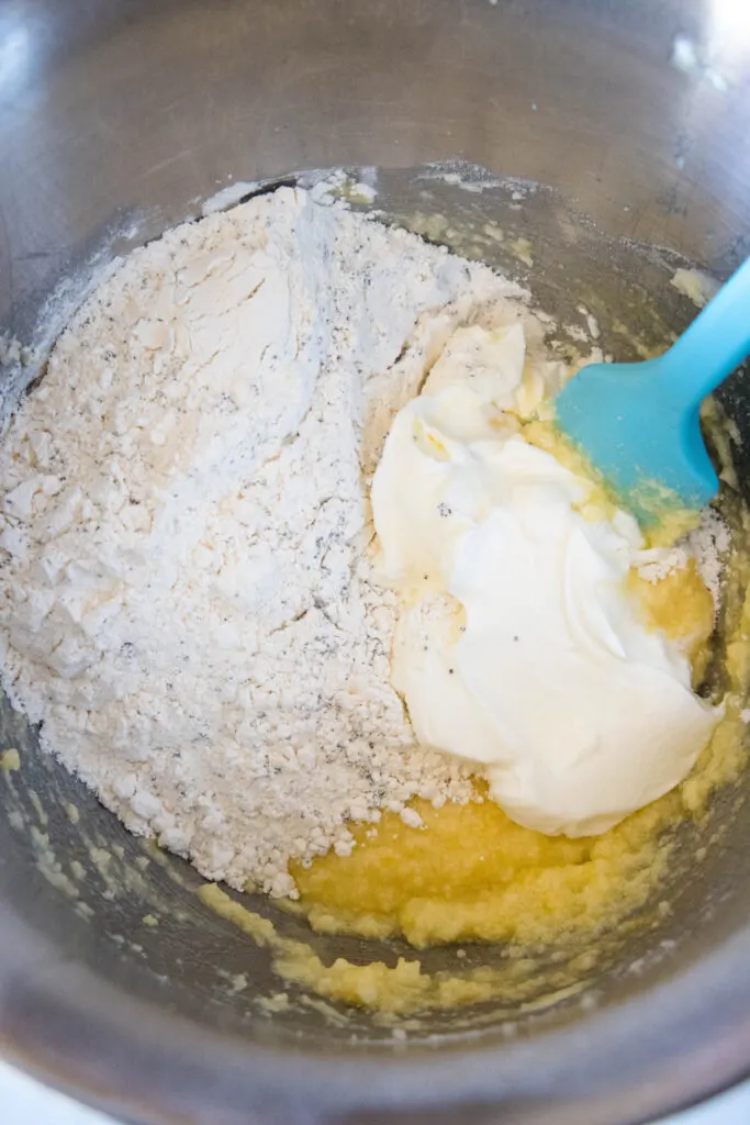 Lemon poppy seed muffin batter ingredients combined in a mixing bowl with a blue rubber spatula.