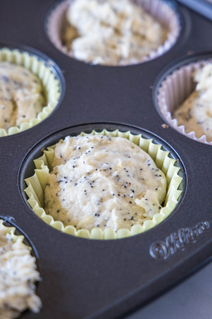 Close up of lined muffin tin wells filled with lemon poppy seed muffin batter.