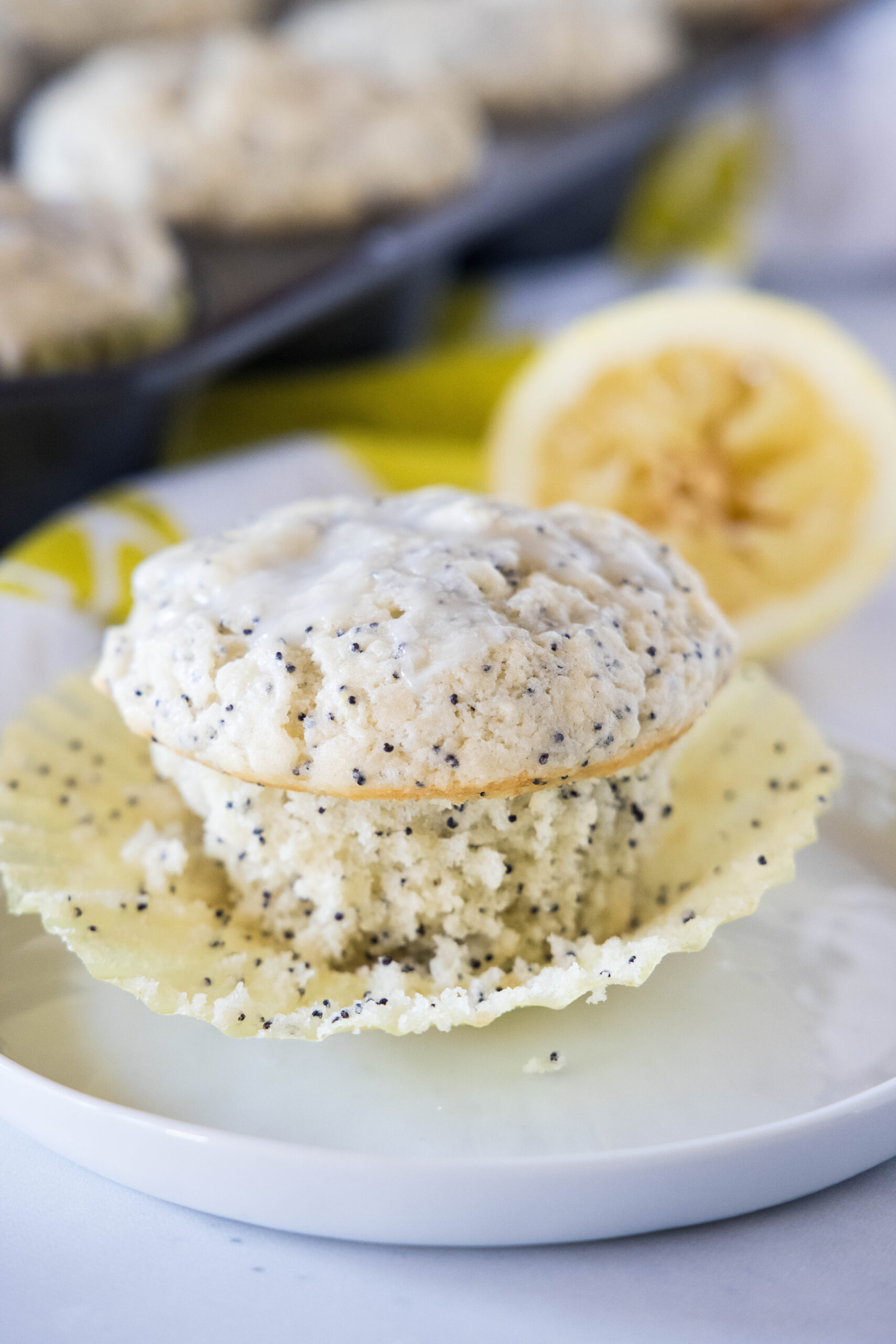 Close up of an unwrapped lemon poppy seed muffin on a white plate.