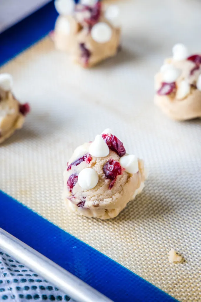 Balls of uncooked cranberry and white chocolate cookie dough on a silpat