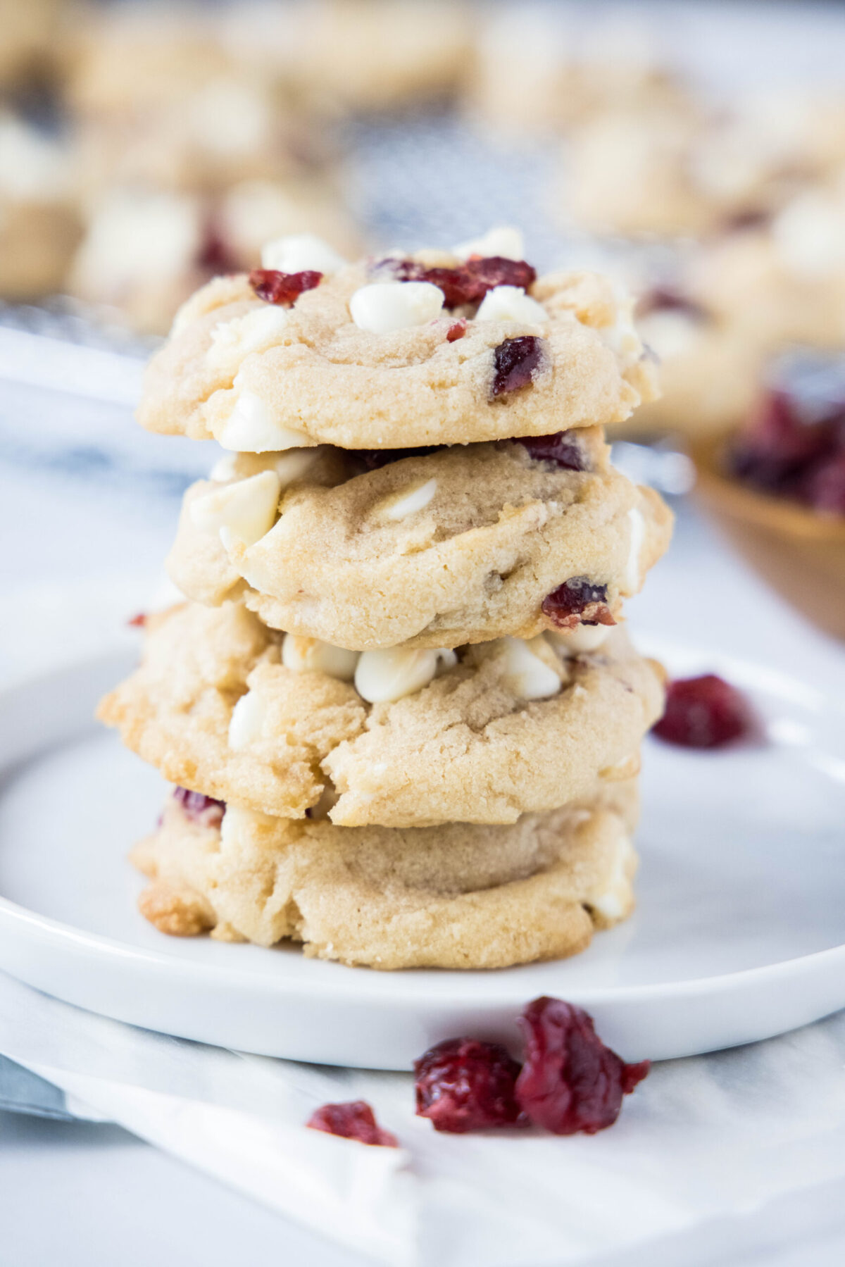 A stack of four white chocolate cranberry cookies on a plate, surrounded by dried cranberries
