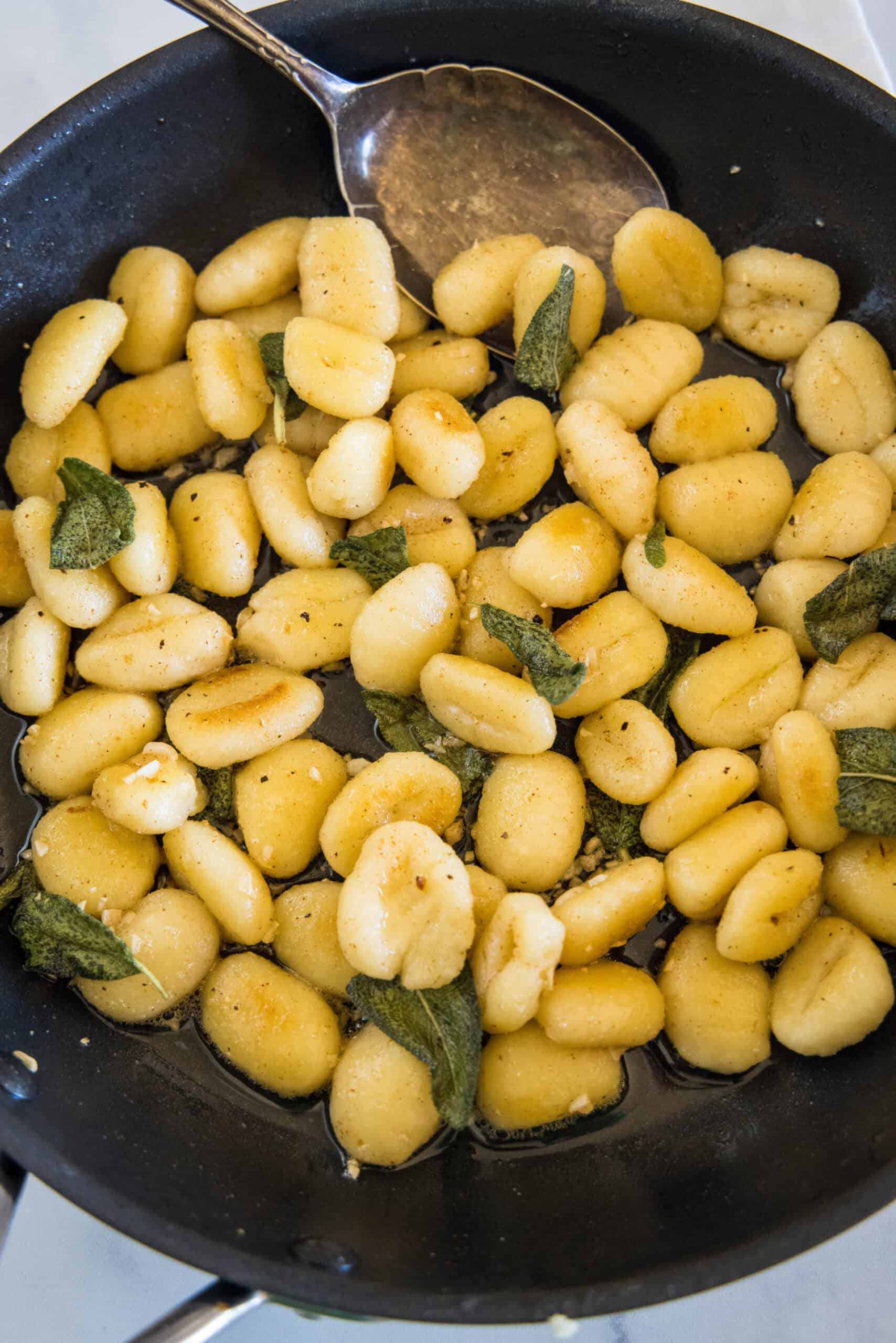 Overhead view of brown butter gnocchi in a skillet with sage leaves.