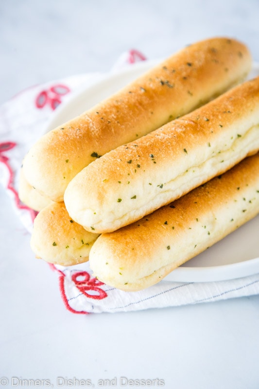 Five breadsticks on a plate, on top of a kitchen towel