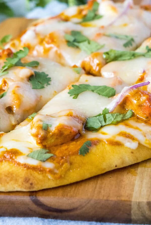 cropped close up sliced chicken tikka pizza on cutting board