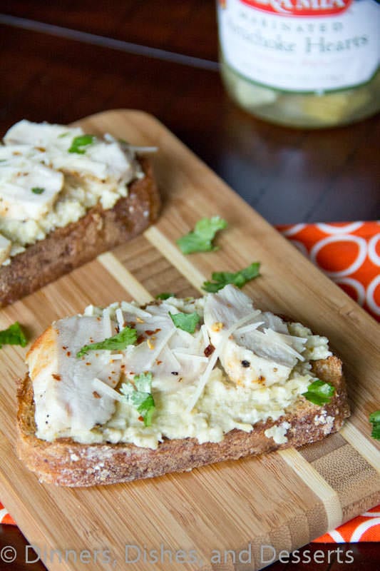 open faced chicken sandwich with artichoke pesto on a board