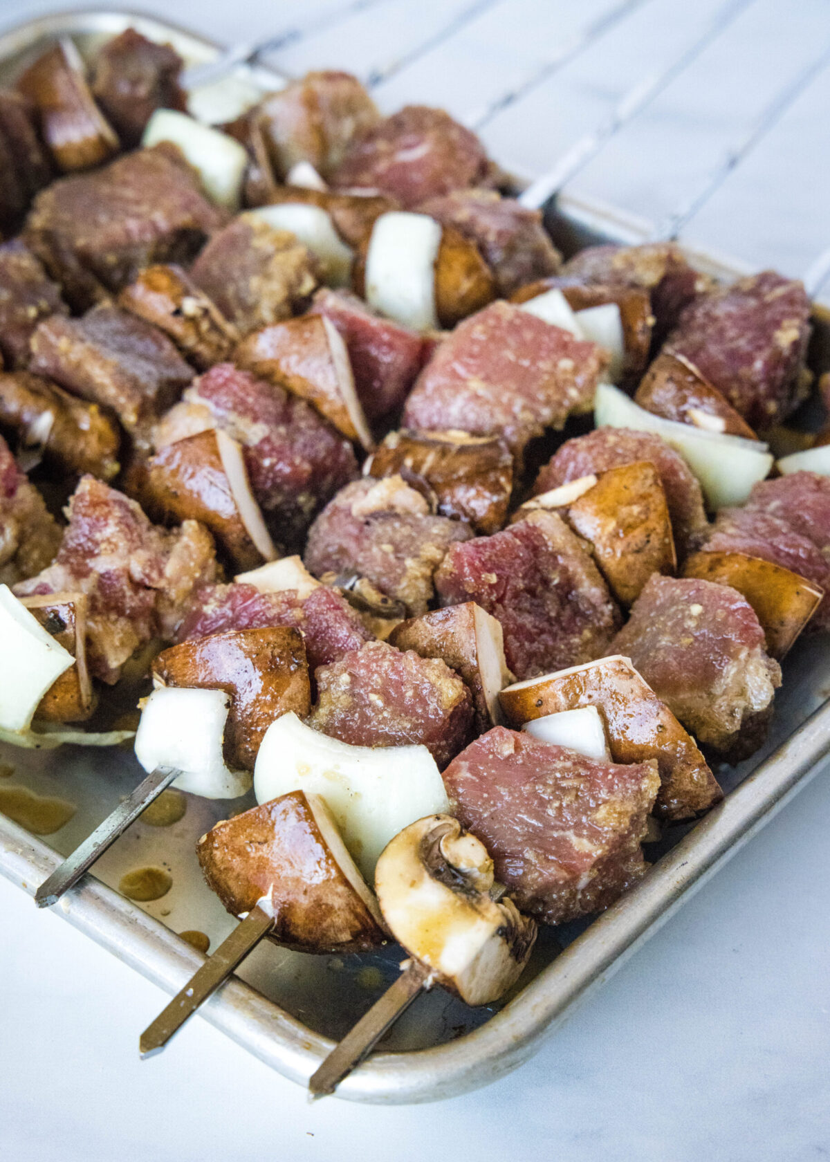A baking sheet full of uncooked beef, onion, and mushroom kabobs