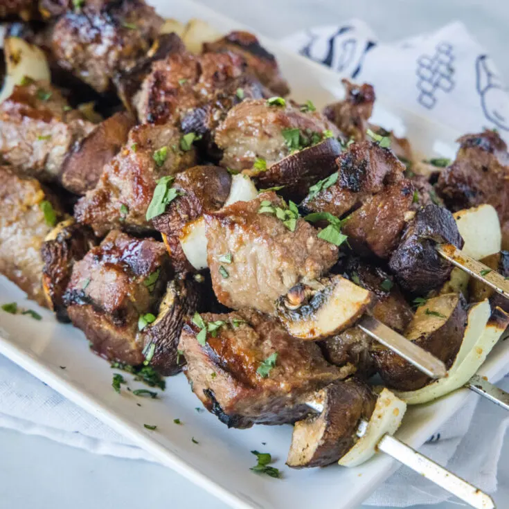 A stack of beef, mushroom, and onion kabobs on a plate