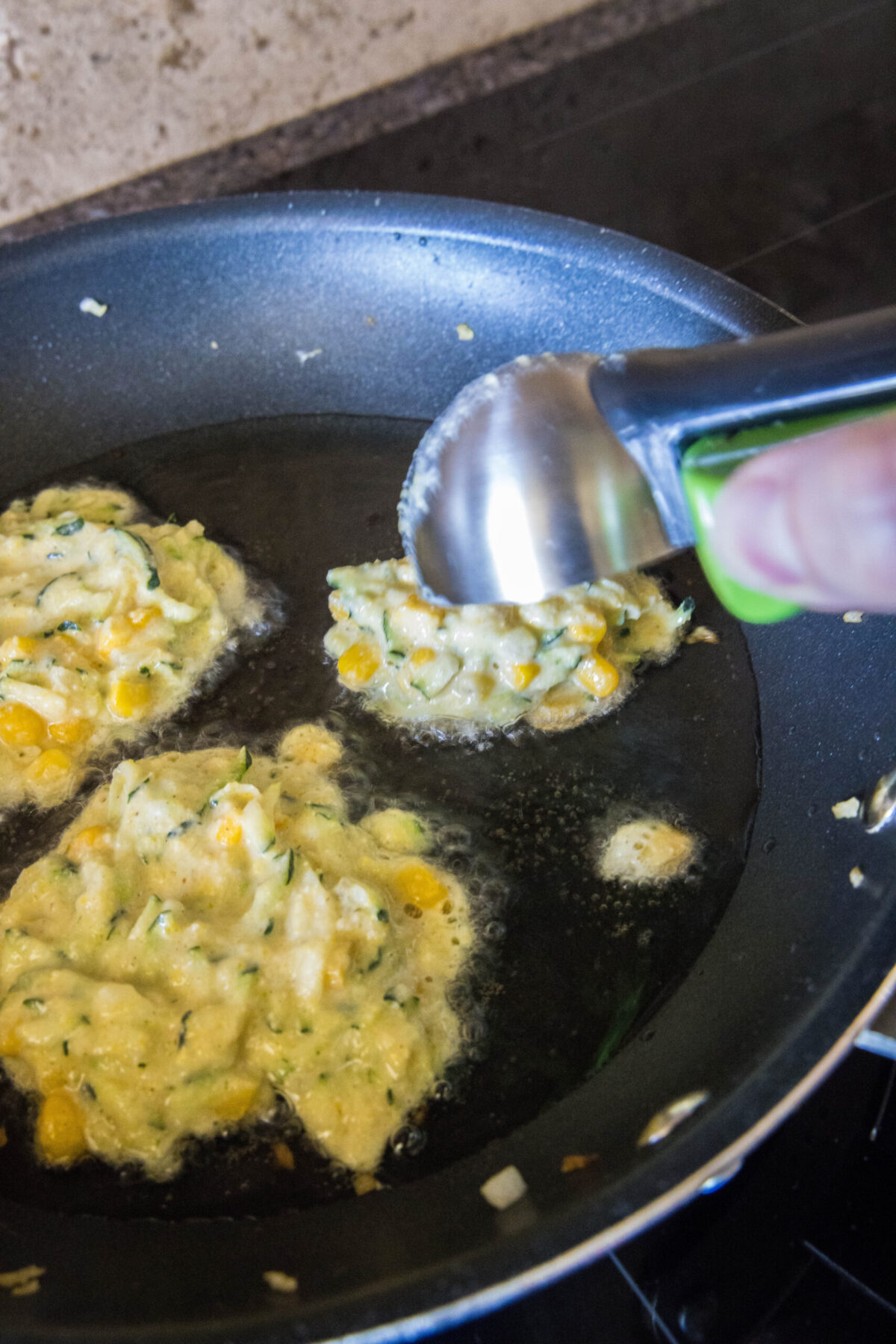 An ice cream scoop dropping zucchini fritter batter into a skillet