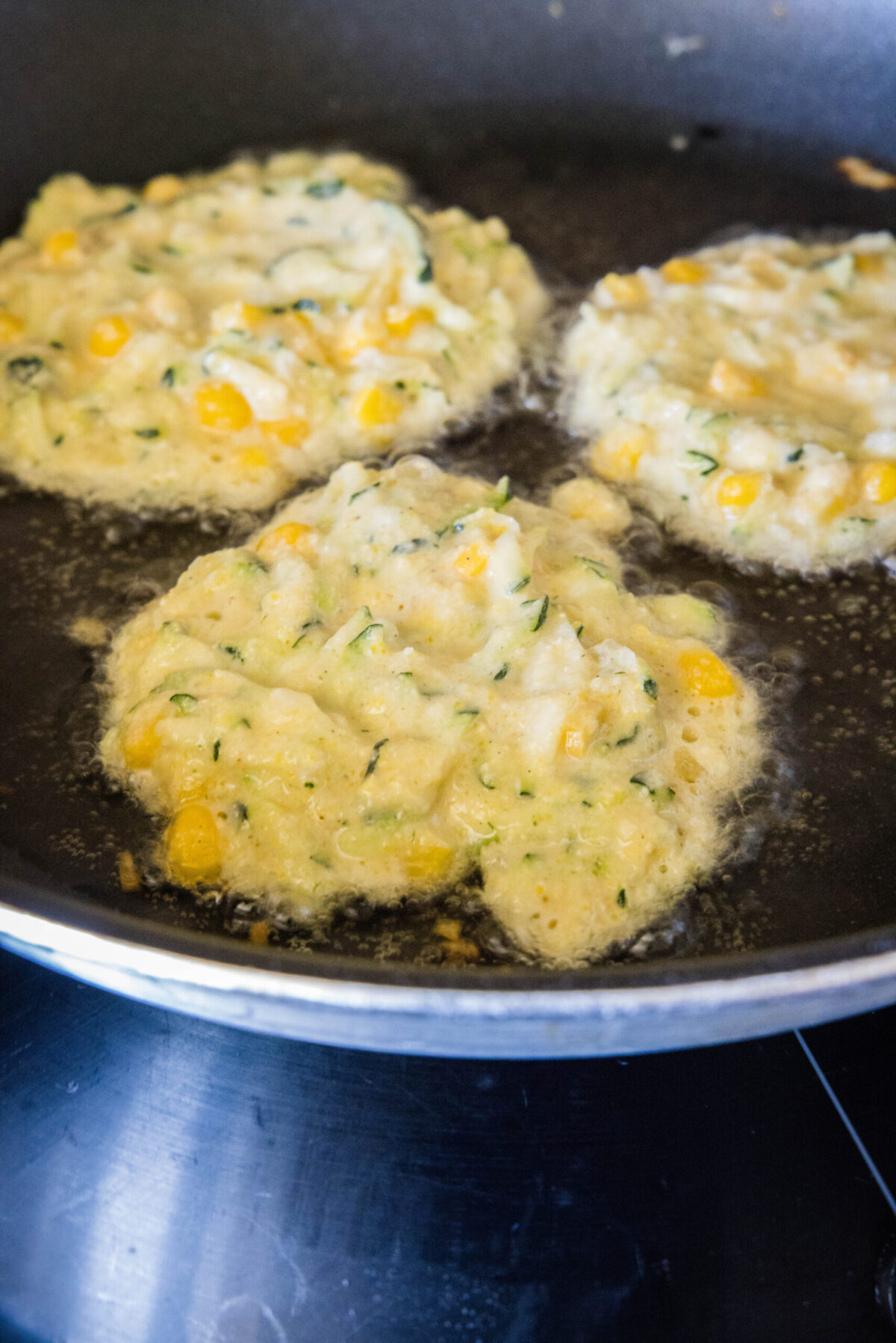 Three raw zucchini fritters cooking in a skillet