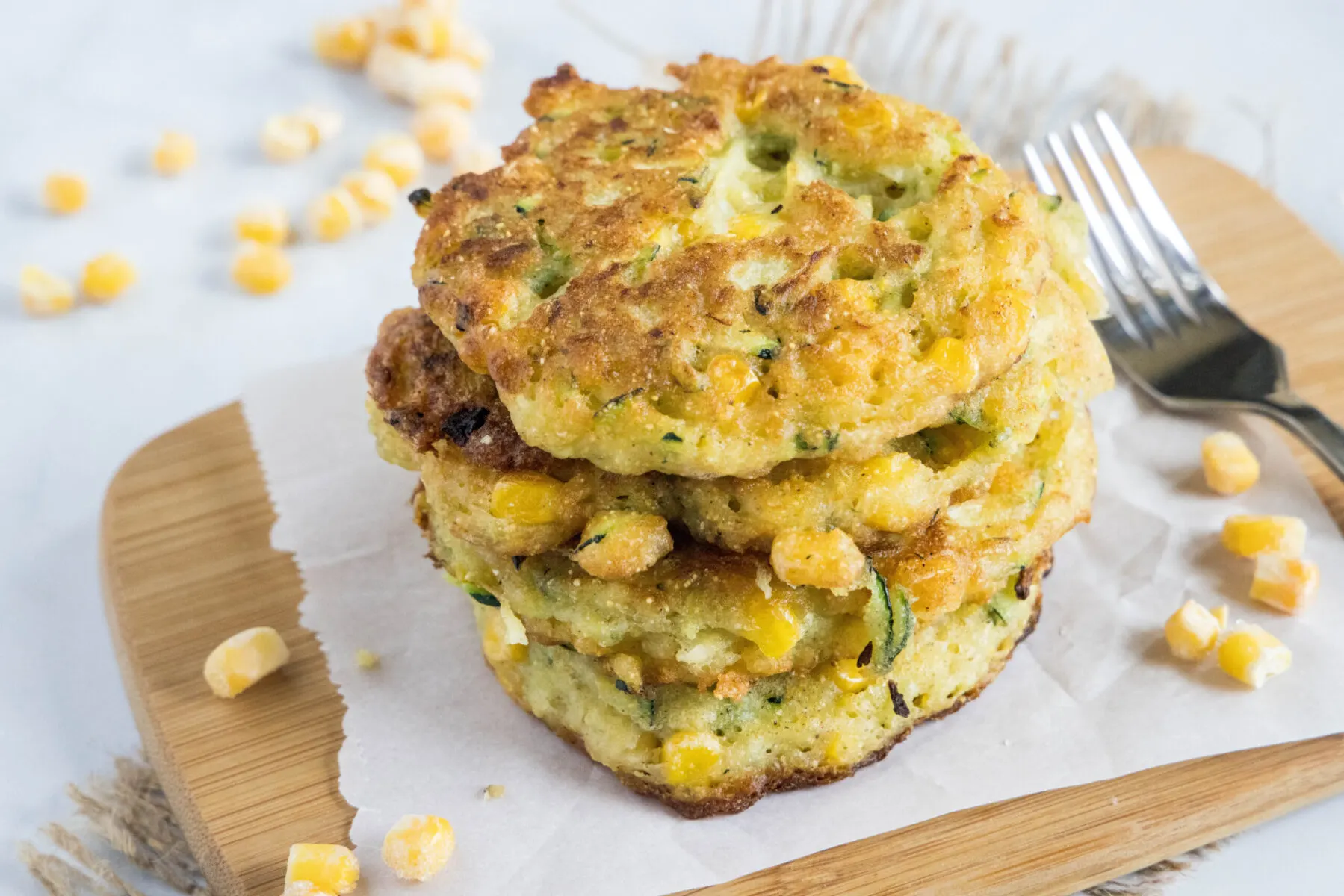 Overhead view of a stack of zucchini fritters surrounded by corn and a fork