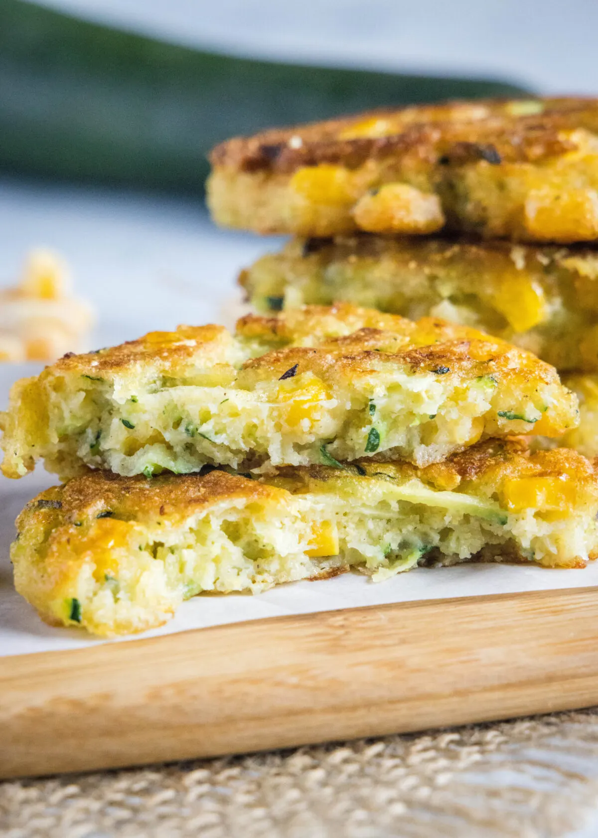 A zucchini fritter broken in half, stacked on top of itself, with a stack of fritters in the background