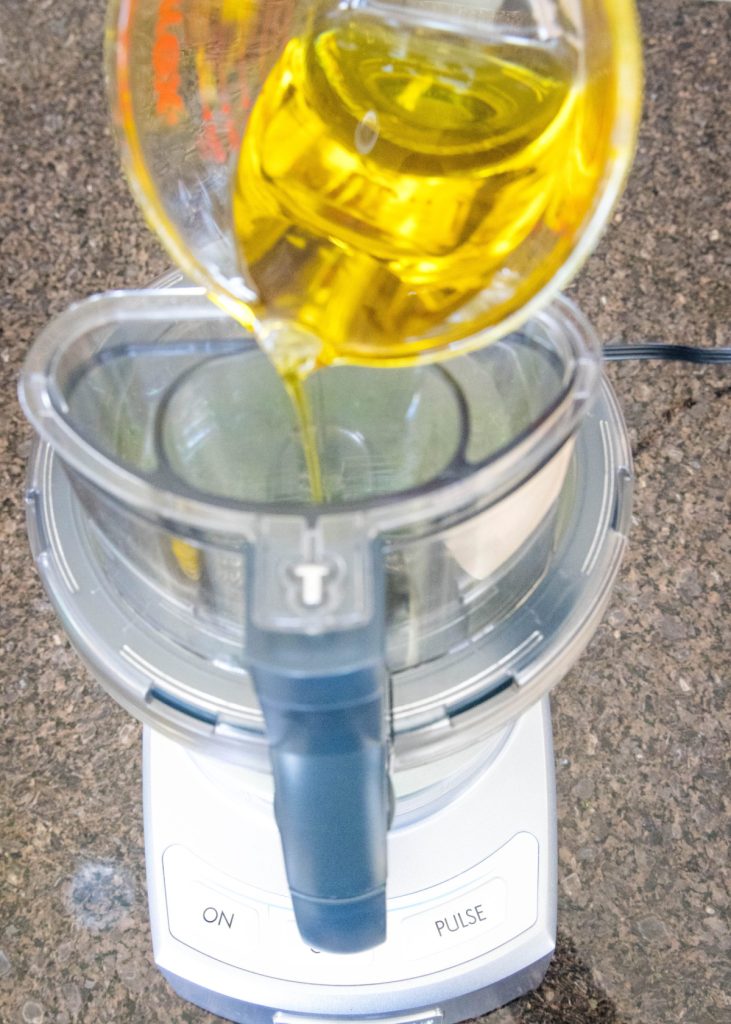A pyrex pouring olive oil into a food processor