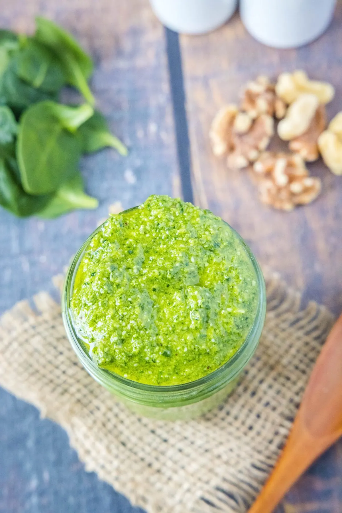 Overhead view of a jar of pesto with spinach and walnuts next to it