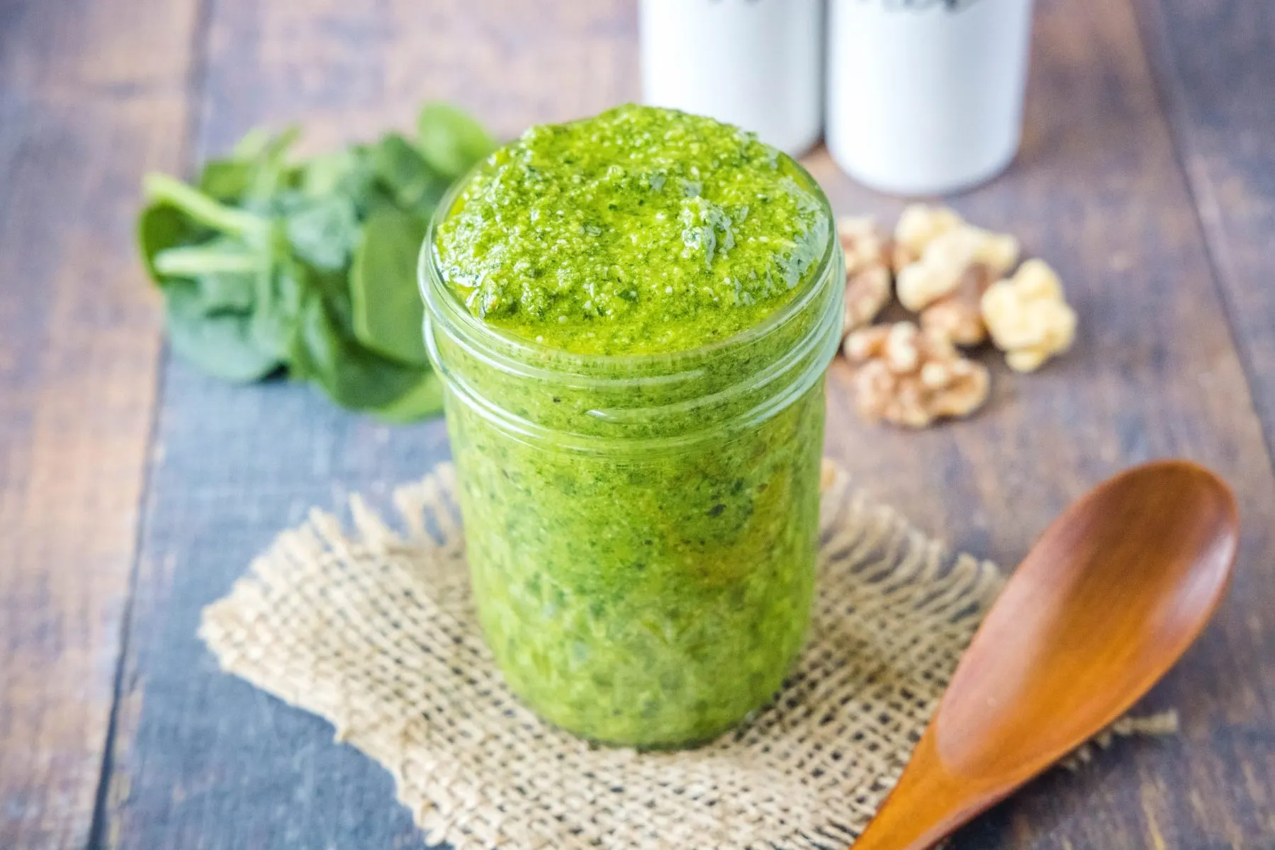 A jar of pesto with walnuts and spinach in the background
