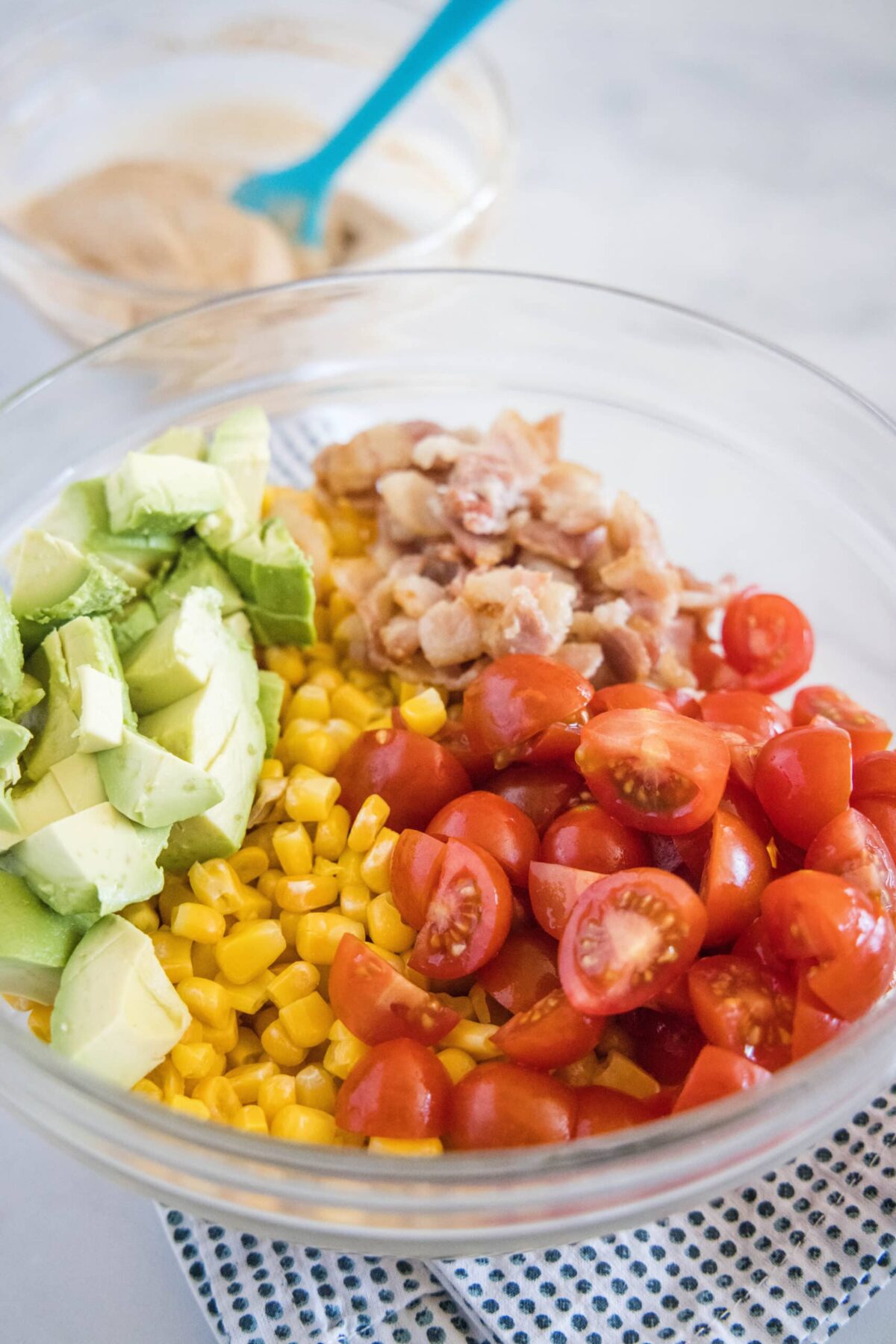 A mixing bowl with quartered cherry tomatoes, corn, pieces of bacon, and avocado