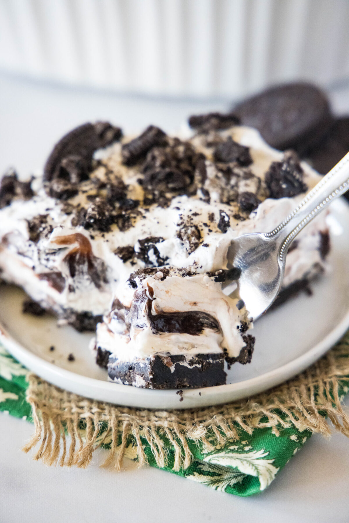 A bite of Oreo squares on a fork, with a plate filled with a slice of Oreo squares in the back