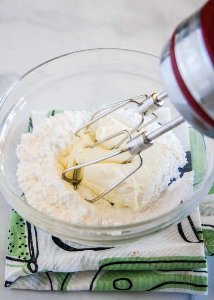 A beater in a bowl with powdered sugar and cream cheese