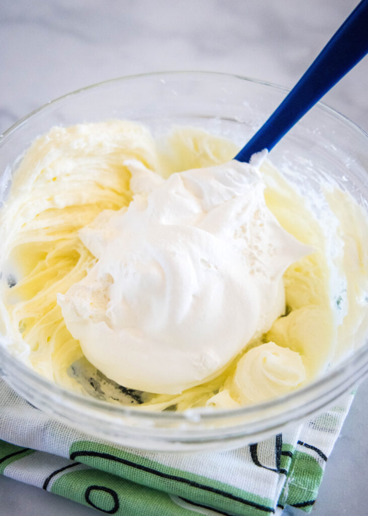 A spatula folding Cool Whip into a cream cheese mixture in a mixing bowl
