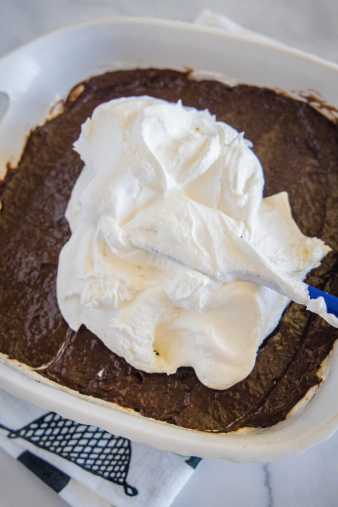 A spatula spreading Cool Whip over chocolate pudding